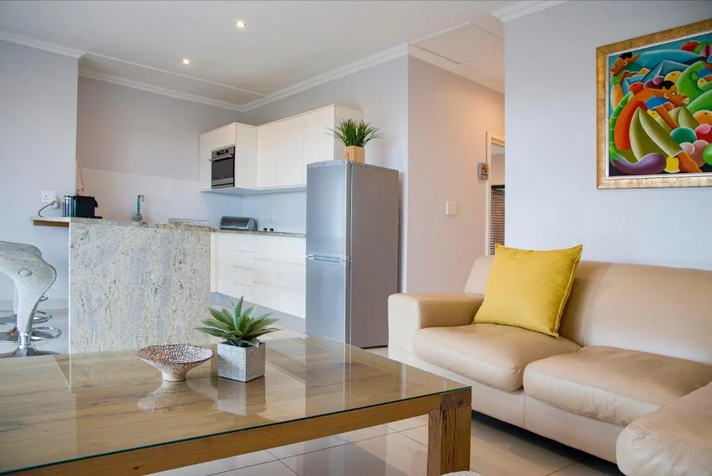 Open-plan lounge with cream sofa and yellow cushion, adjacent to modern kitchen