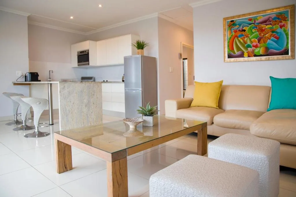 Modern lounge with beige sofa, colorful artwork, and open-plan kitchen behind