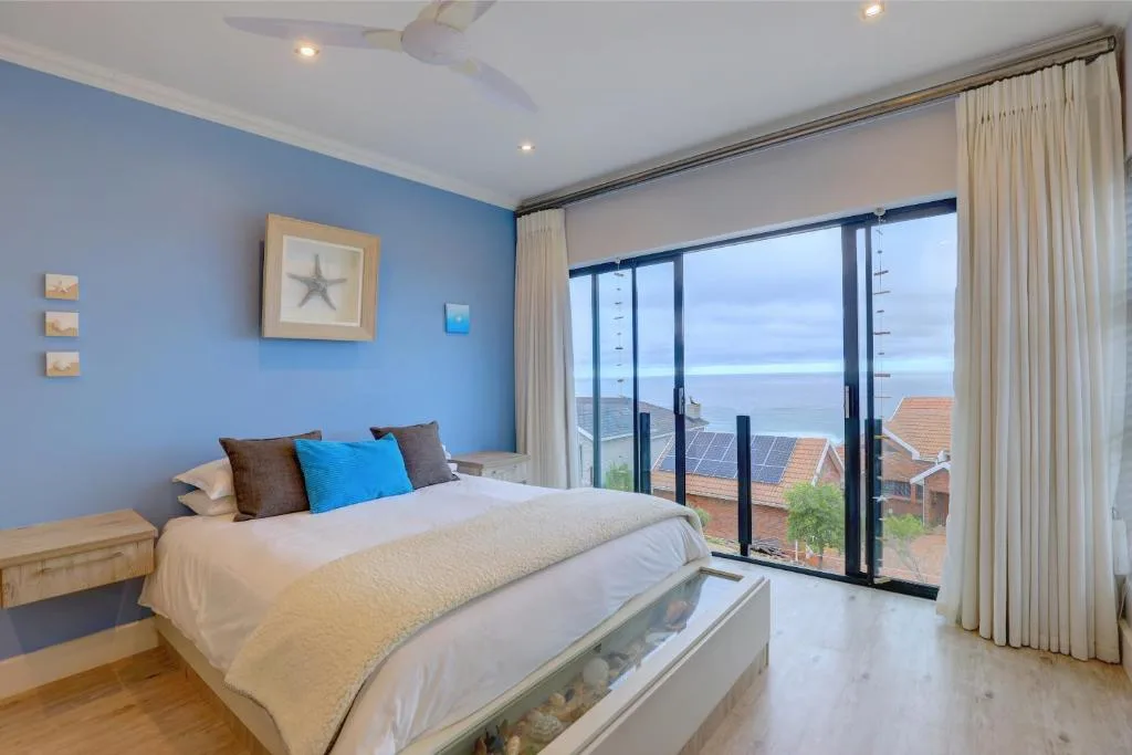 Bright bedroom with ocean view through sliding glass doors and blue accent wall