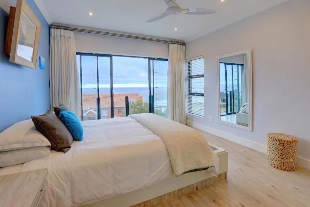 Bright modern bedroom with ocean view through large windows and coastal landscape beyond