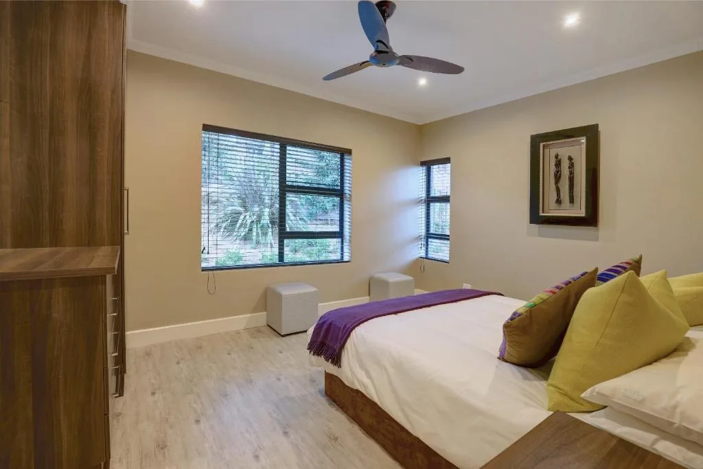 Bright bedroom with twin beds, yellow pillows, ceiling fan, and garden views