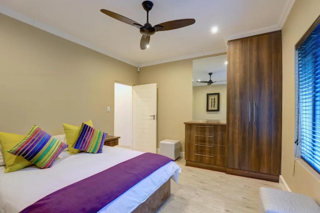 Bright bedroom with colorful pillows, wooden wardrobe, and ceiling fan