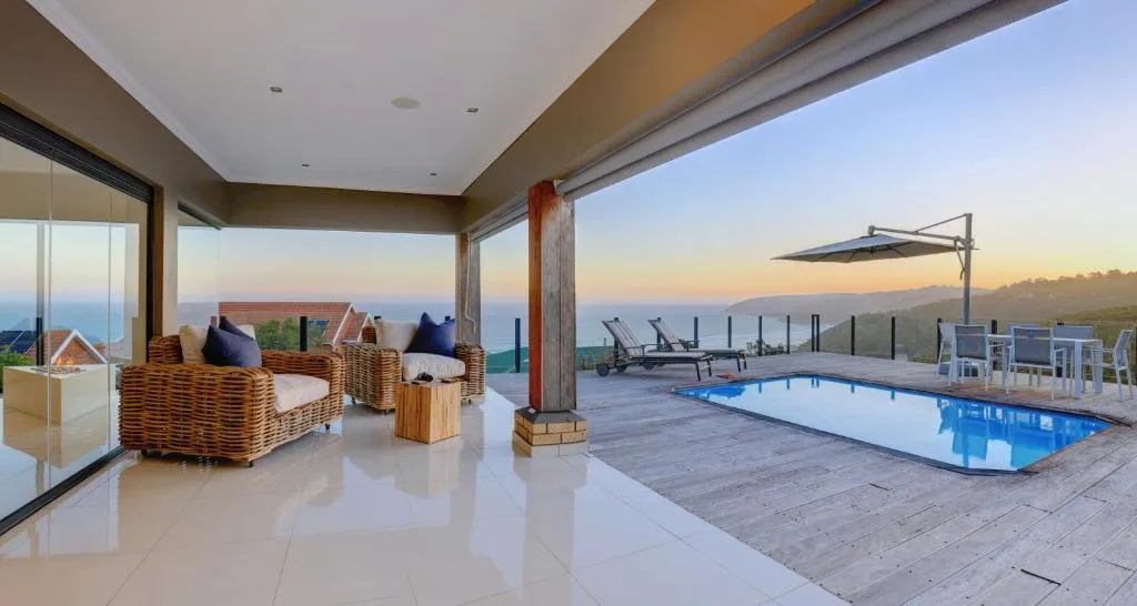 Expansive outdoor deck with pool, seating, and ocean views at sunset