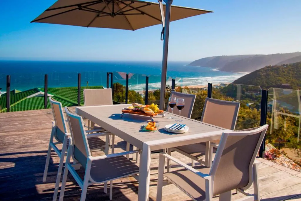 Outdoor dining table with ocean and mountain views under umbrella