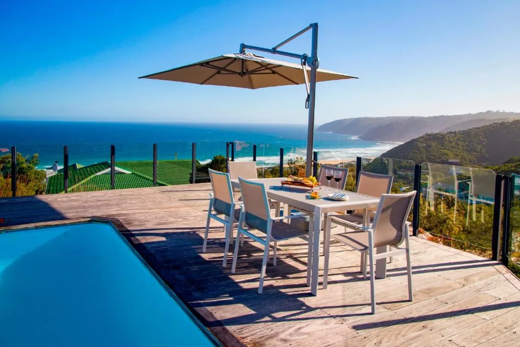 Oceanview deck with dining table, umbrella, and swimming pool overlooking Garden Route coastline