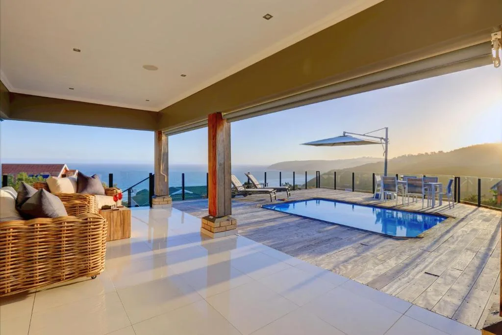 Covered deck with lounge seating overlooking ocean and swimming pool area