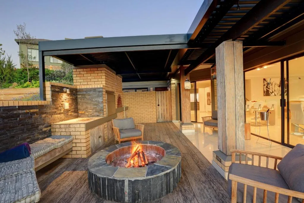 Covered outdoor patio with fire pit, seating, and braai area at dusk