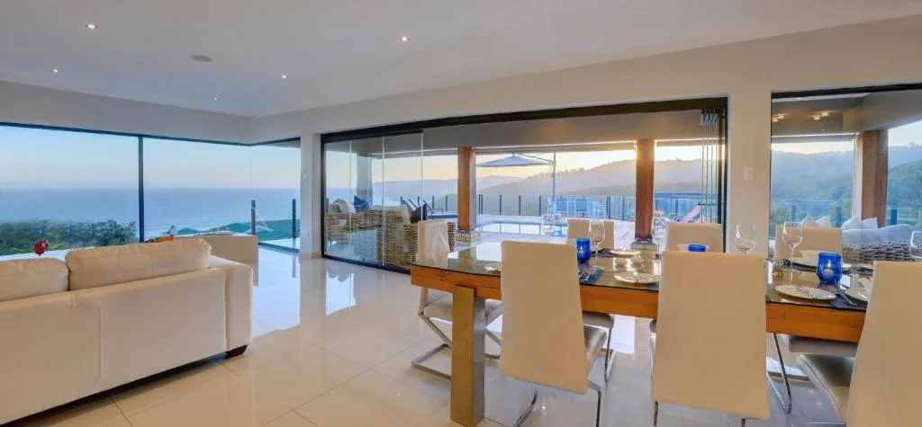 Open-plan lounge and dining area with panoramic ocean and mountain views through floor-to-ceiling windows