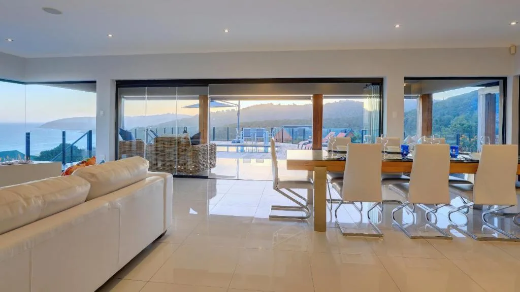 Open-plan lounge and dining area with mountain and ocean views through glass doors