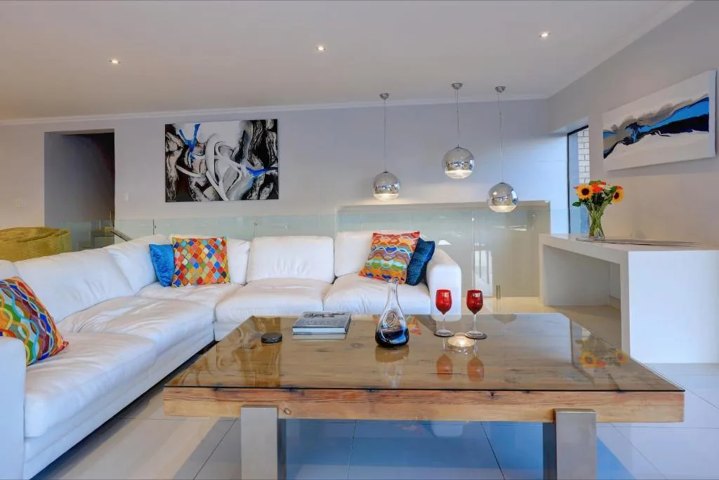 Modern lounge with white sectional sofa, colorful cushions, pendant lights, and wooden coffee table