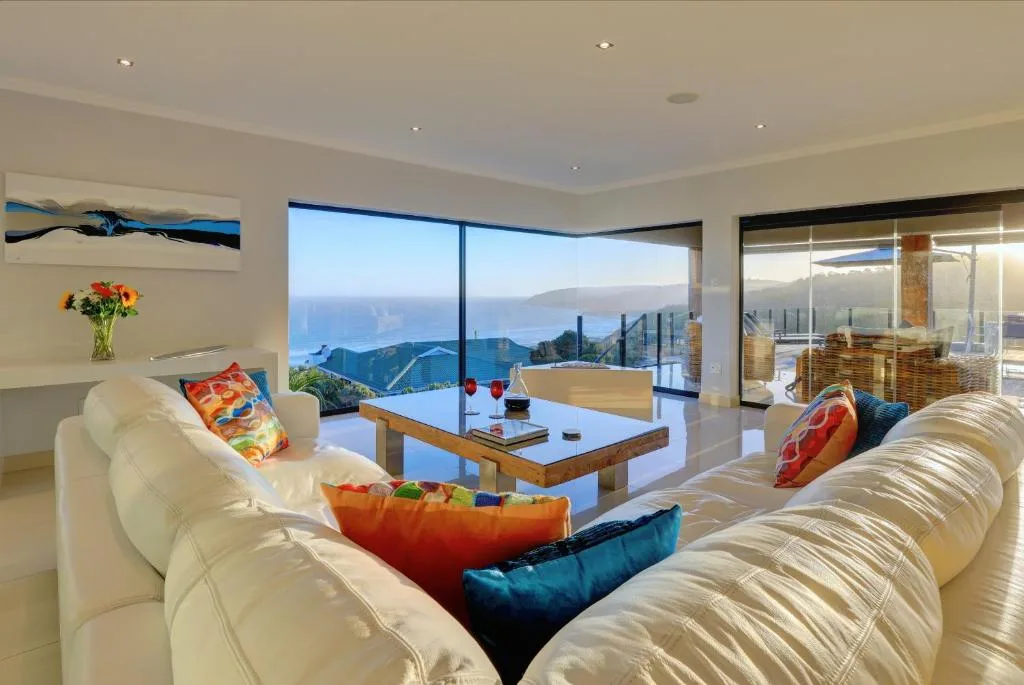 Spacious lounge with cream sofas overlooking coastal mountain views through large windows