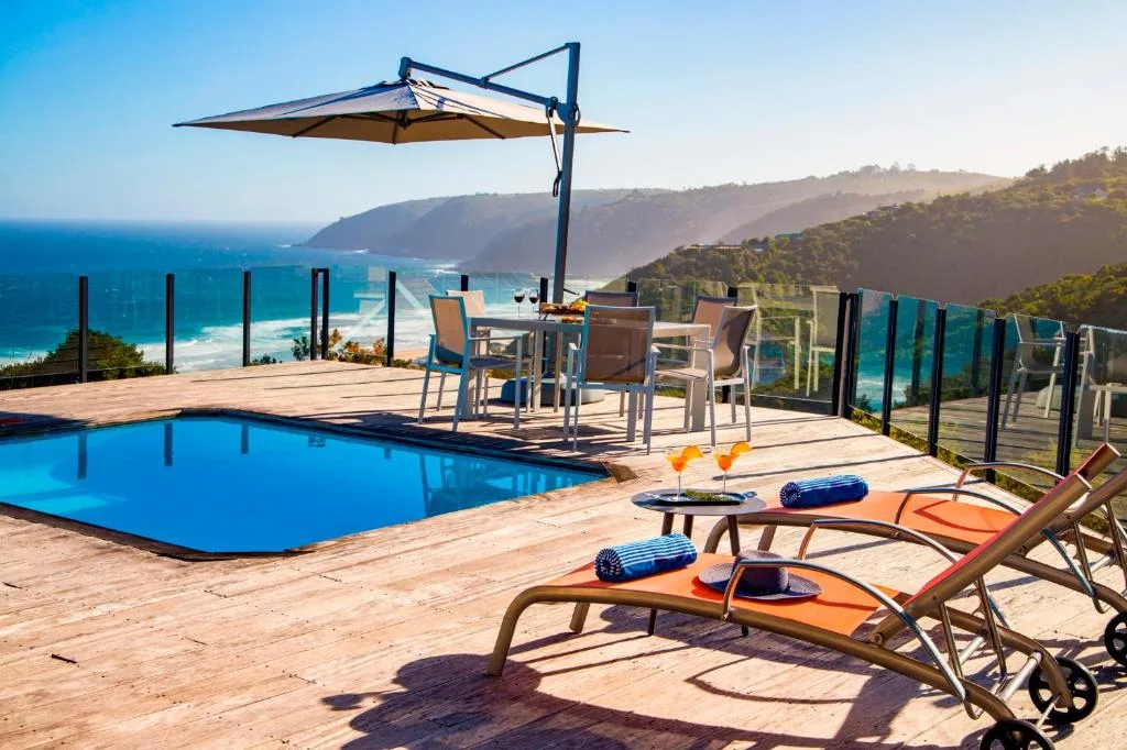 Swimming pool with lounge chairs and umbrella overlooking coastal cliffs