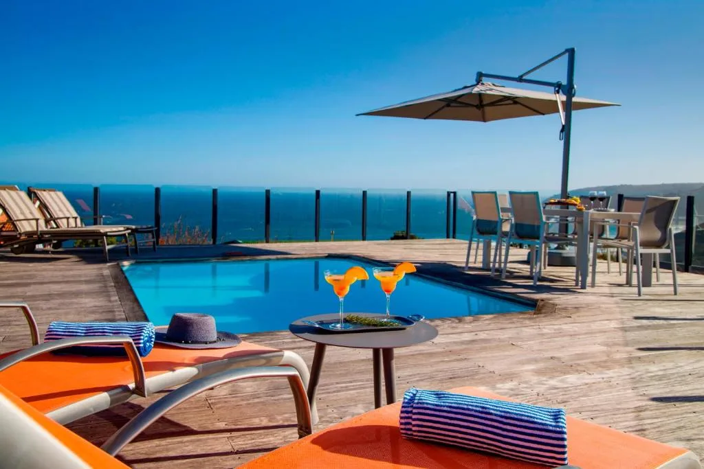 Sparkling blue pool with ocean view, loungers, umbrella, and cocktails