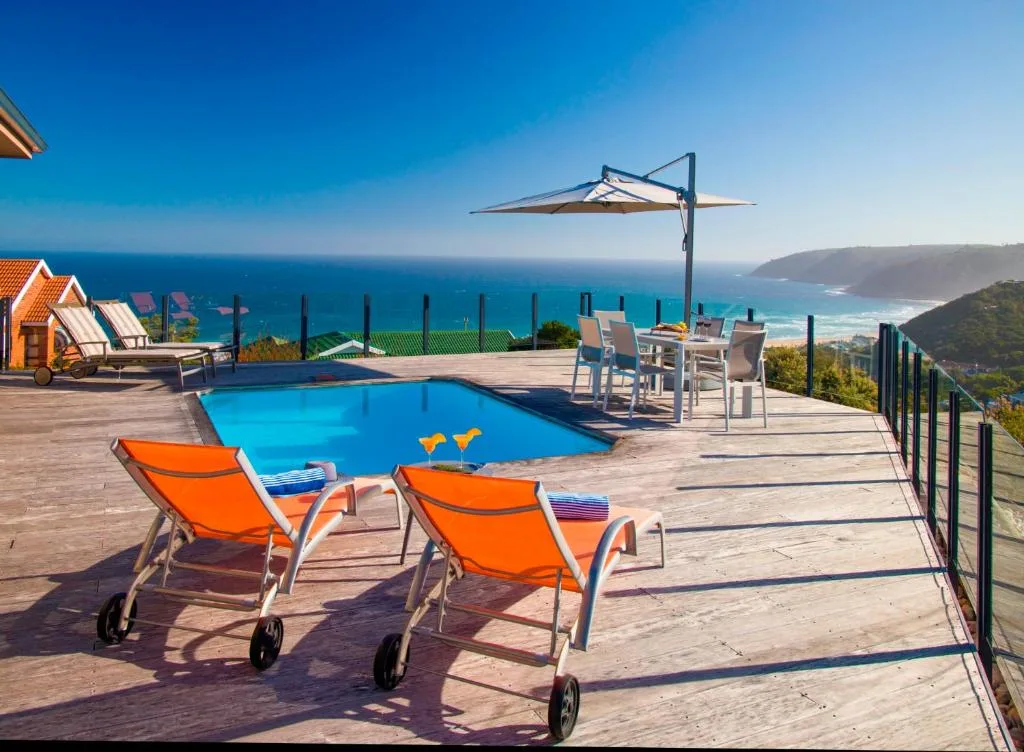 Swimming pool with loungers and ocean views on wooden deck
