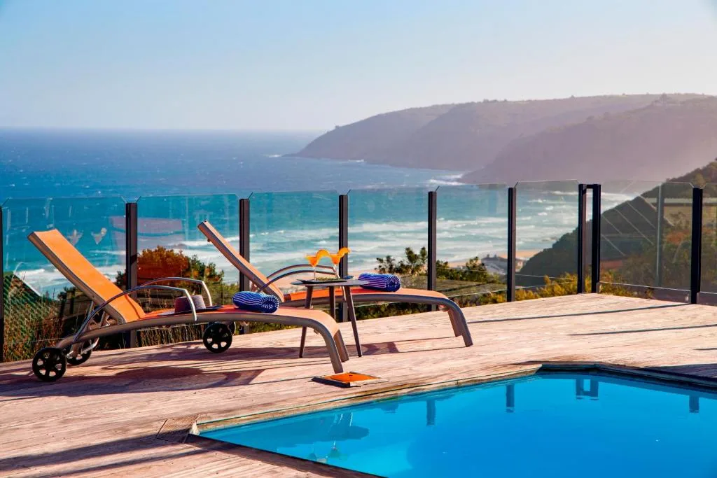 Swimming pool with ocean and coastal cliffs visible beyond glass railing