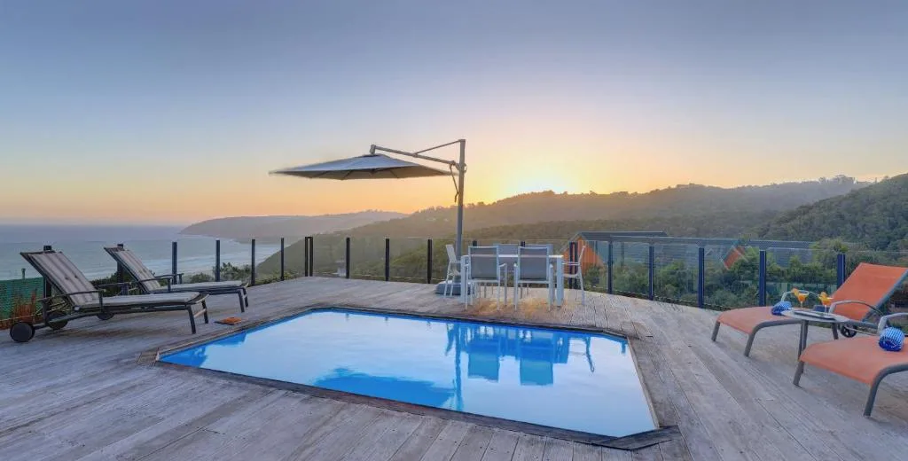Illuminated swimming pool at sunset with ocean and mountain views beyond