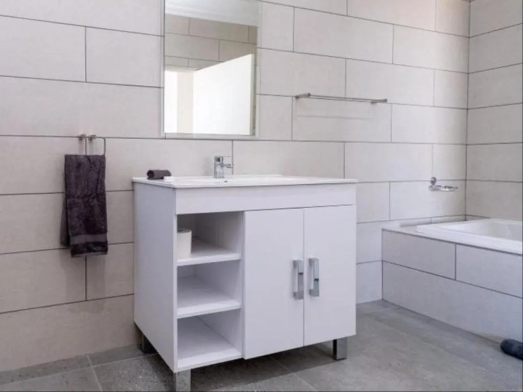 Modern bathroom with white tile walls, vanity sink, mirror, and bathtub
