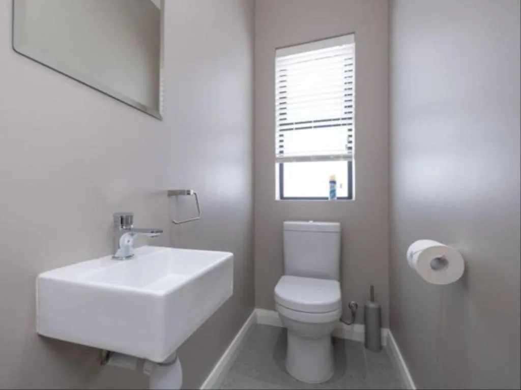 Modern bathroom with white sink, toilet, and window with blinds