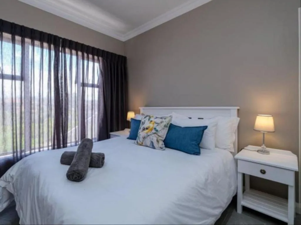 Bright bedroom with white bed, blue pillows, and dark curtains