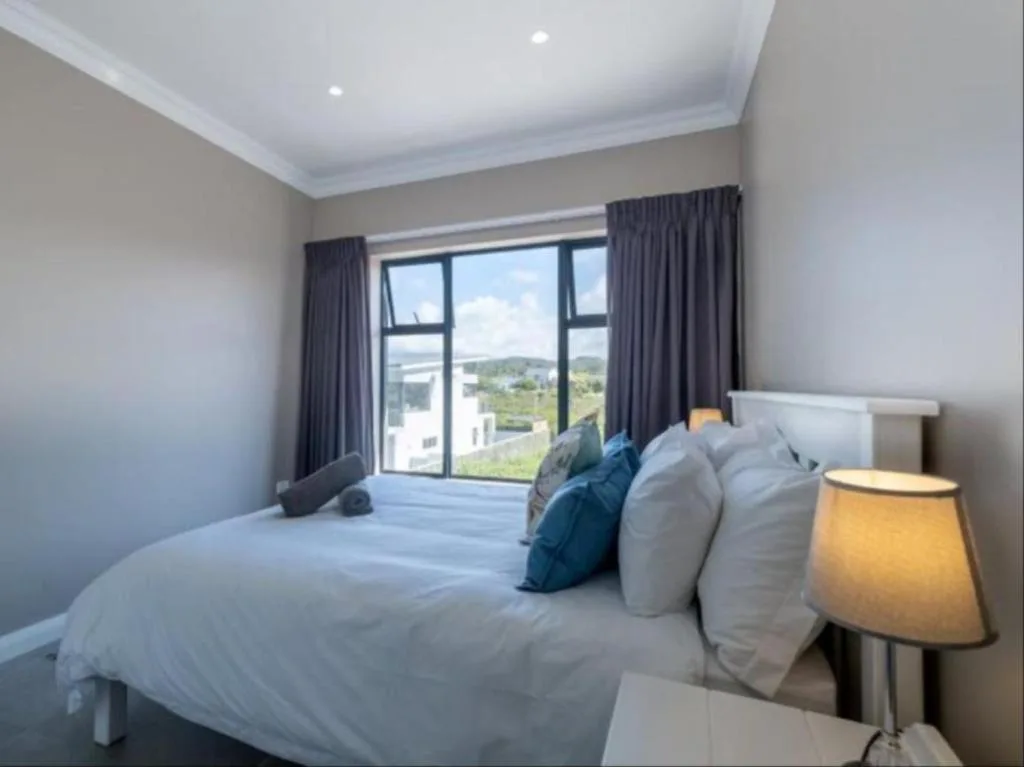 Bright bedroom with white bedding, blue accents, and mountain views through large windows