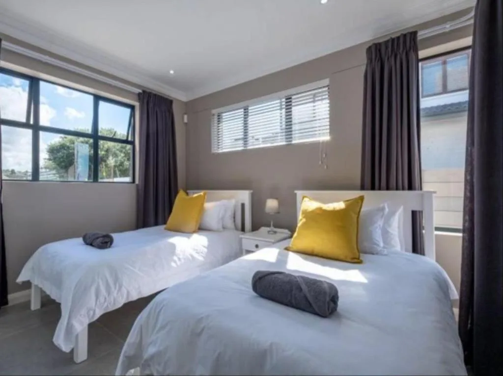 Bright bedroom with two single beds, yellow accent pillows, and garden views
