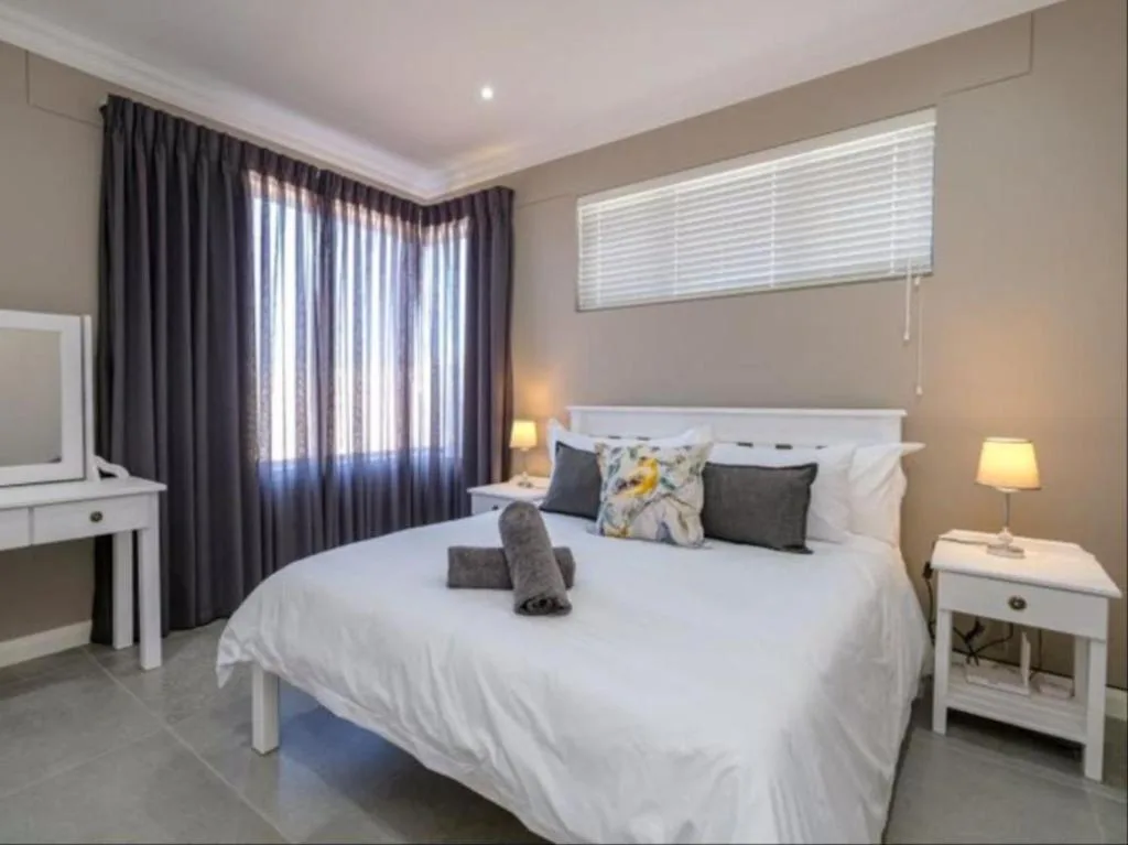 Spacious bedroom with queen bed, white bedside tables, and dark curtains