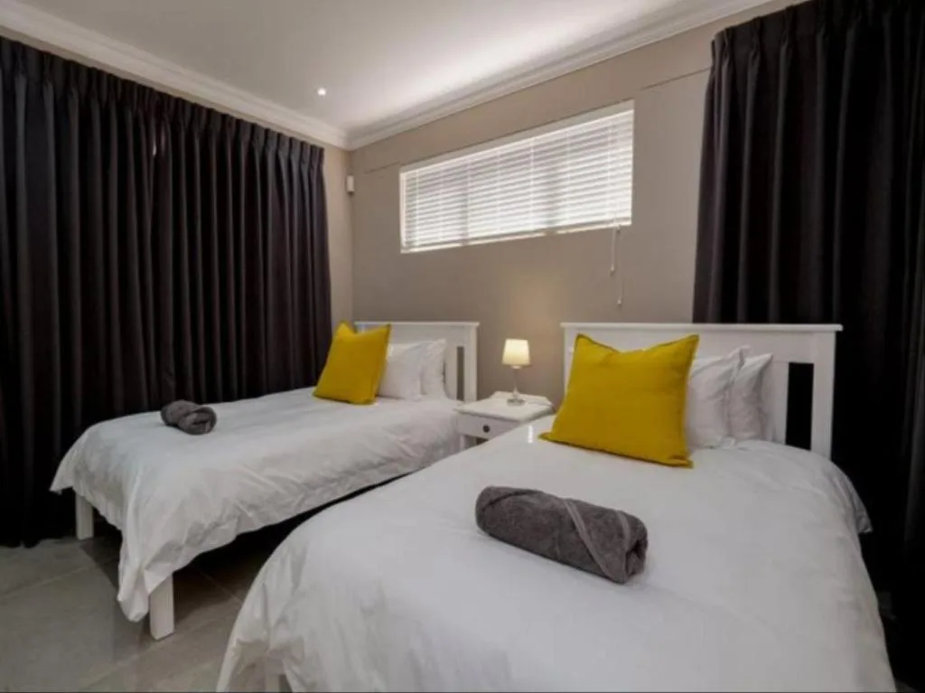 Twin bedroom with white beds, yellow pillows, dark curtains, modern lighting