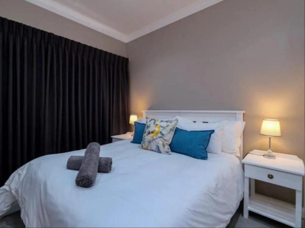 Modern bedroom with white bed, blue pillows, dark curtains, bedside lamp