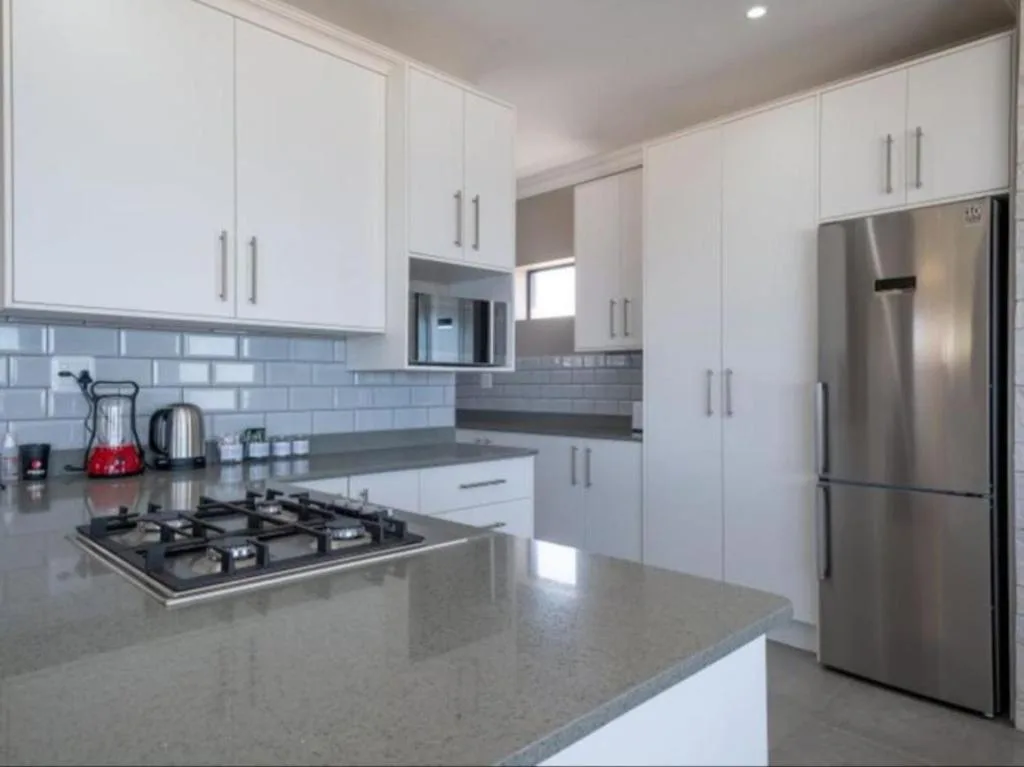 Modern white kitchen with gas cooktop, stainless steel appliances, gray countertops
