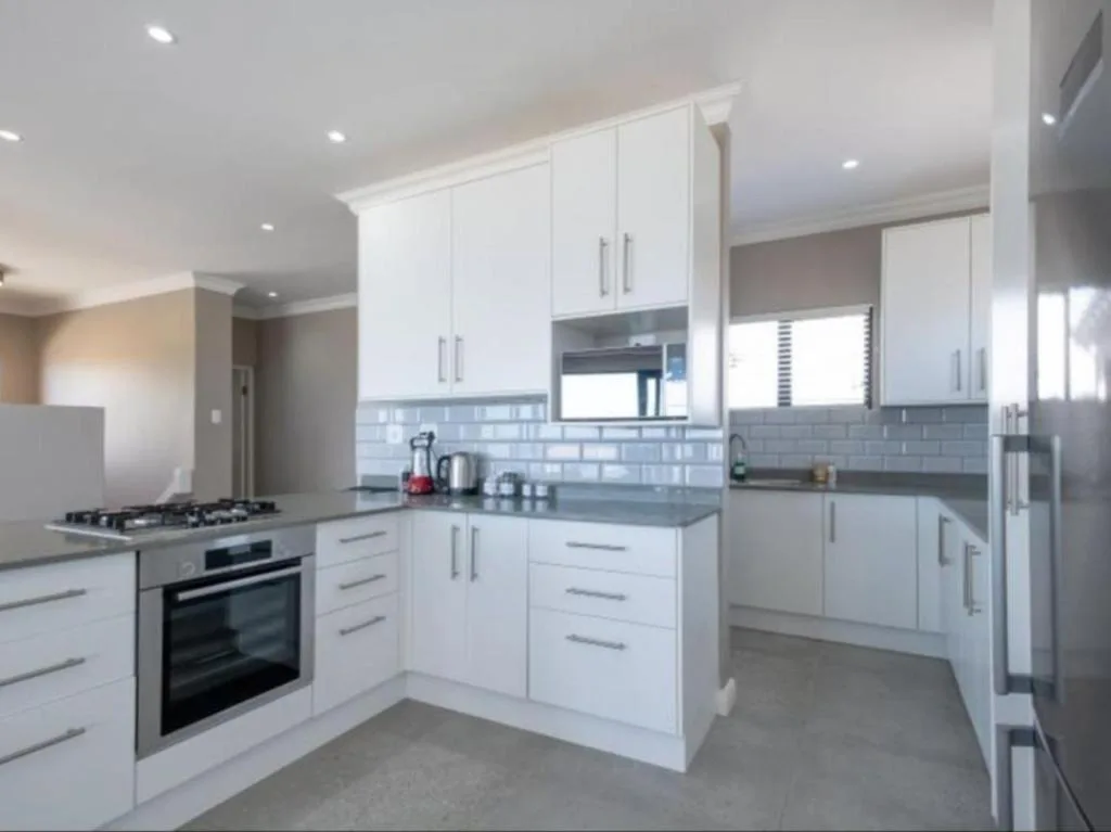Modern white kitchen with gas stove, grey subway tile backsplash, and stainless steel appliances