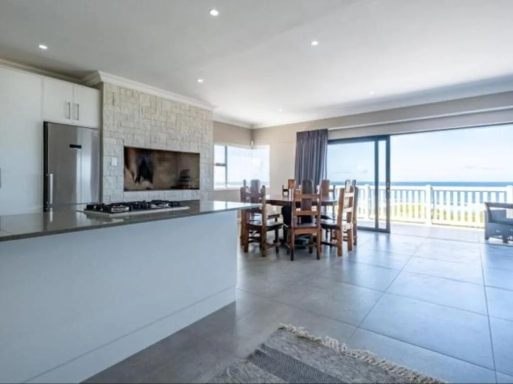 Modern open-plan lounge with kitchen, dining area and ocean views through glass doors