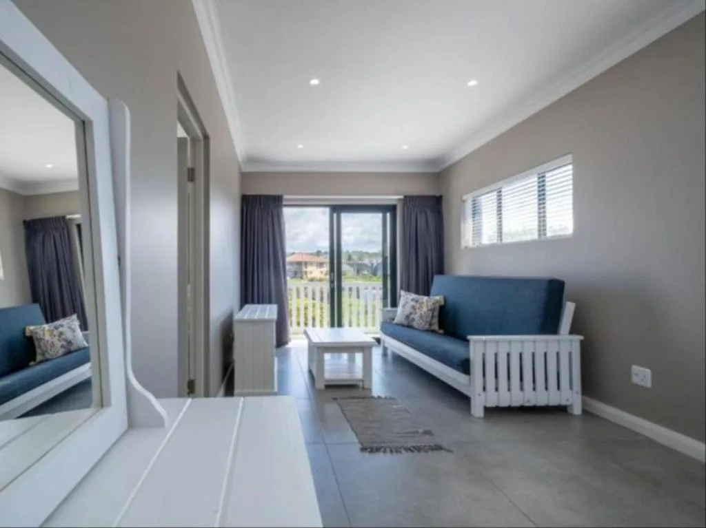 Bright lounge with blue sofa, large mirror, and deck access overlooking gardens