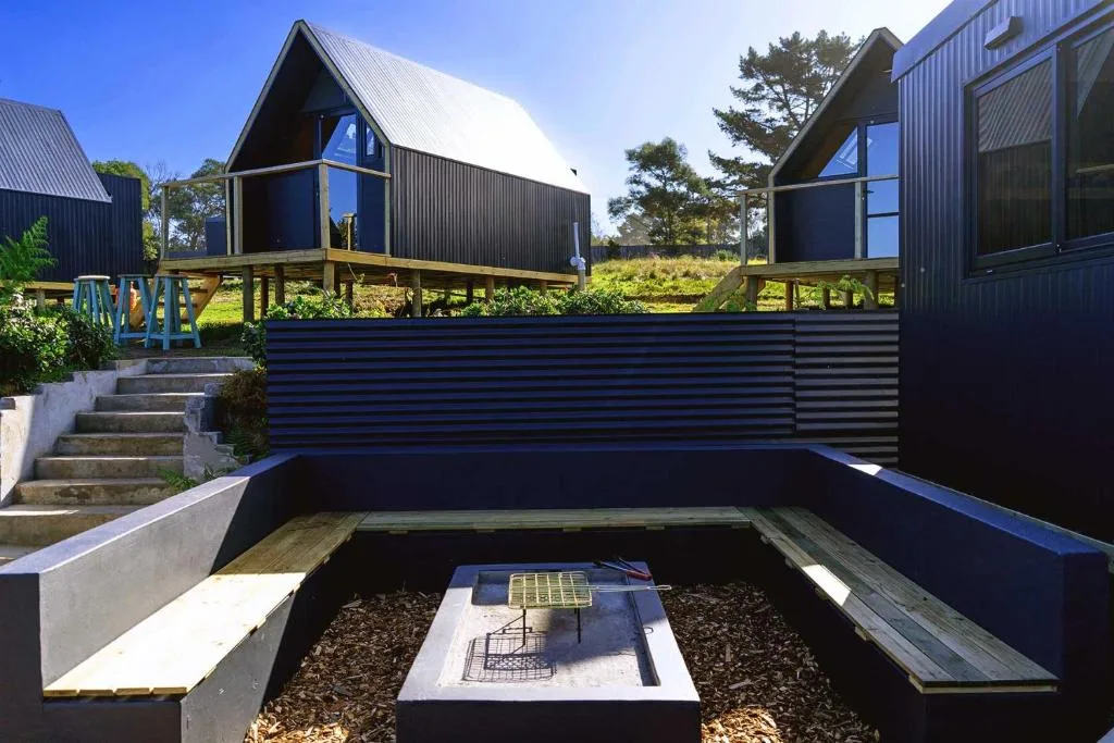 Modern black A-frame glamping pods with elevated decks overlooking green countryside