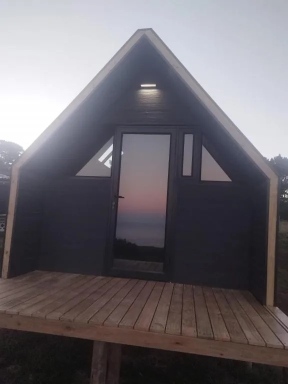 Modern black A-frame glamping cabin with wooden deck at dusk