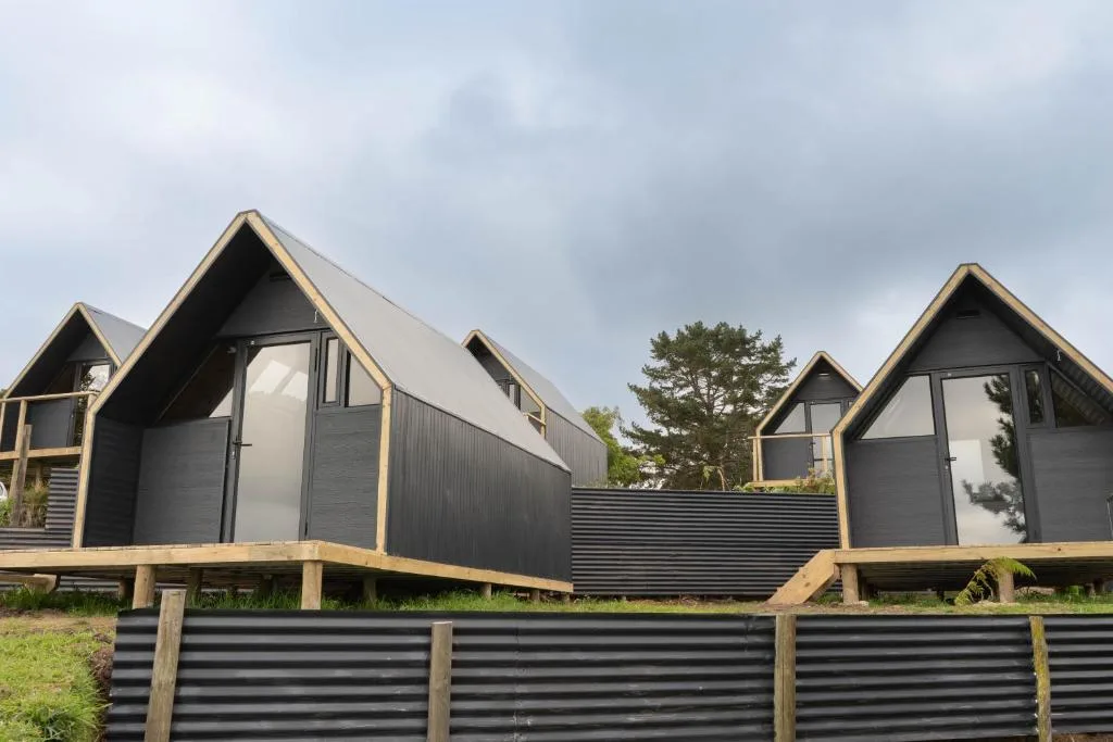 Modern black and timber glamping pods with peaked roofs and wooden decks