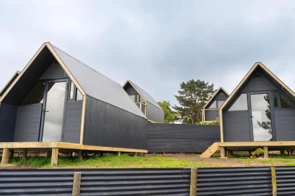 Modern black and gold A-frame glamping units with wooden decks in Wilderness
