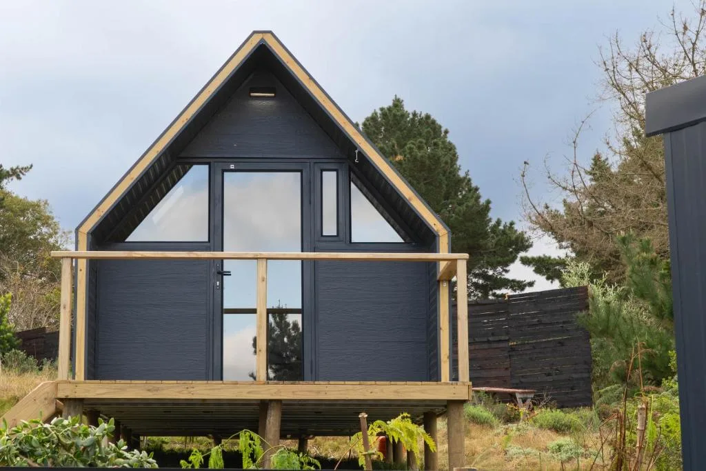 Modern A-frame glamping cottage with dark exterior and wooden deck platform