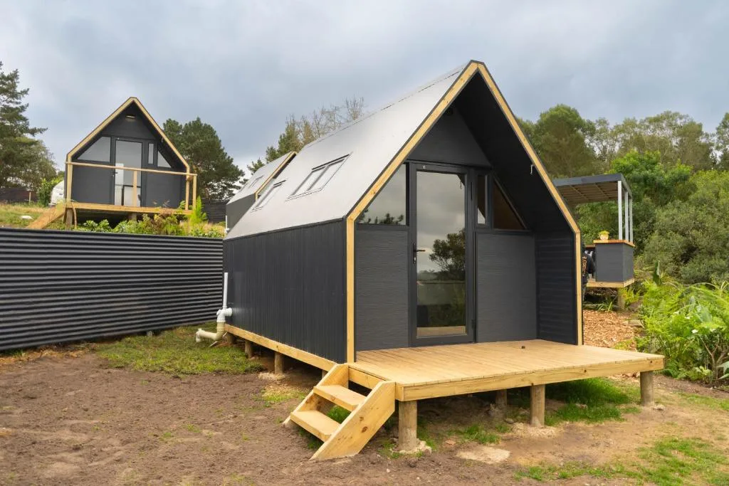 Modern black and gold A-frame glamping cabin with wooden deck and steps