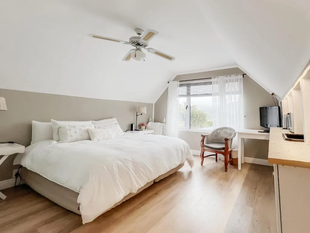 Bright bedroom with white bedding, ceiling fan, and large window