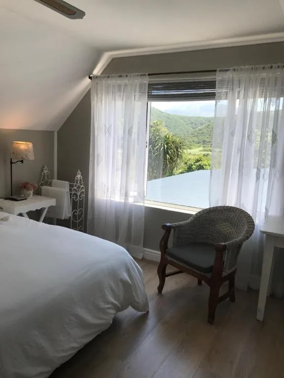 Bright bedroom with white bed, chair, and lush mountain view through windows