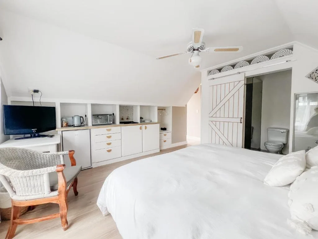 Bright bedroom with white bed, kitchenette, and en-suite bathroom in loft space