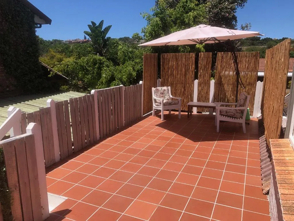 Spacious outdoor patio with terracotta tiles, wooden fence, umbrella, and seating