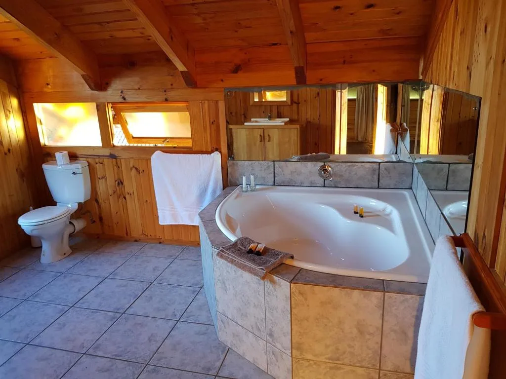 Spacious bathroom with sunken bathtub, toilet, vanity, and wooden beams