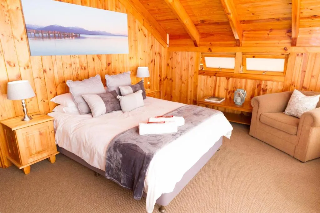 Spacious wooden bedroom with queen bed, armchair, and scenic lagoon artwork