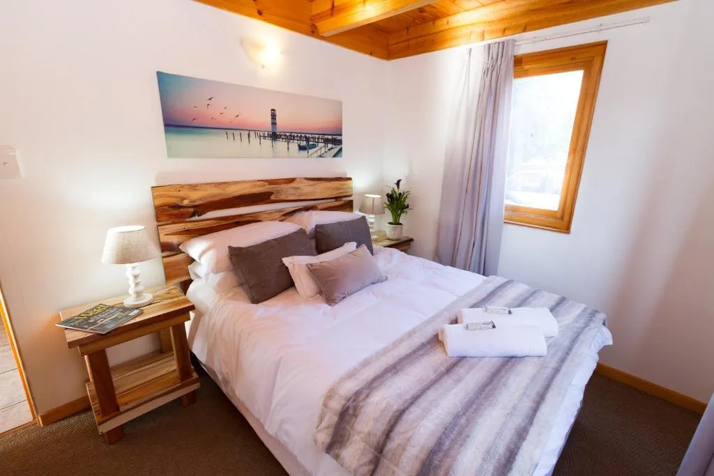 Bright bedroom with wooden headboard, quality linens, bedside lamp and coastal artwork.