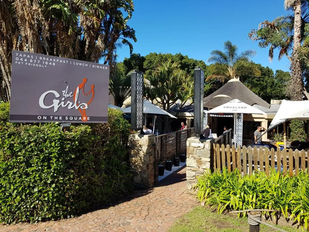 Restaurant entrance with signage, tropical landscaping, and outdoor dining area