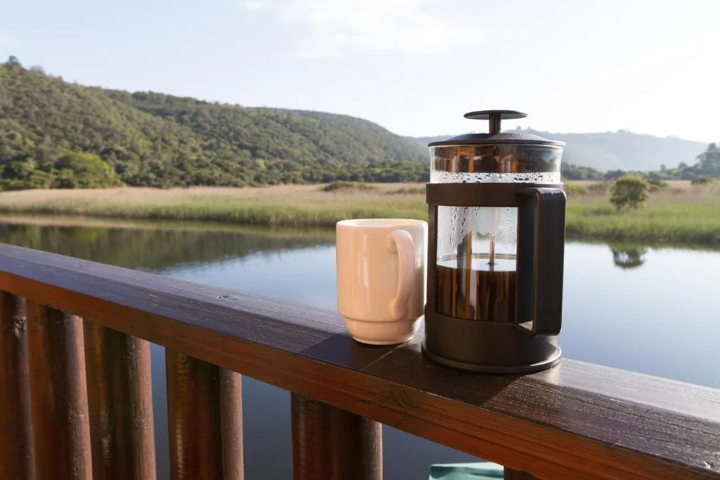 Coffee on wooden deck overlooking tranquil river and forested mountains