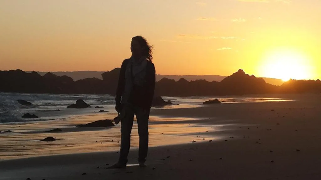 Golden sunset over rocky coastline with dramatic mountain silhouettes and ocean