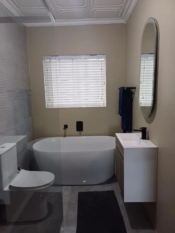 Modern bathroom with freestanding tub, toilet, vanity sink, and round mirror
