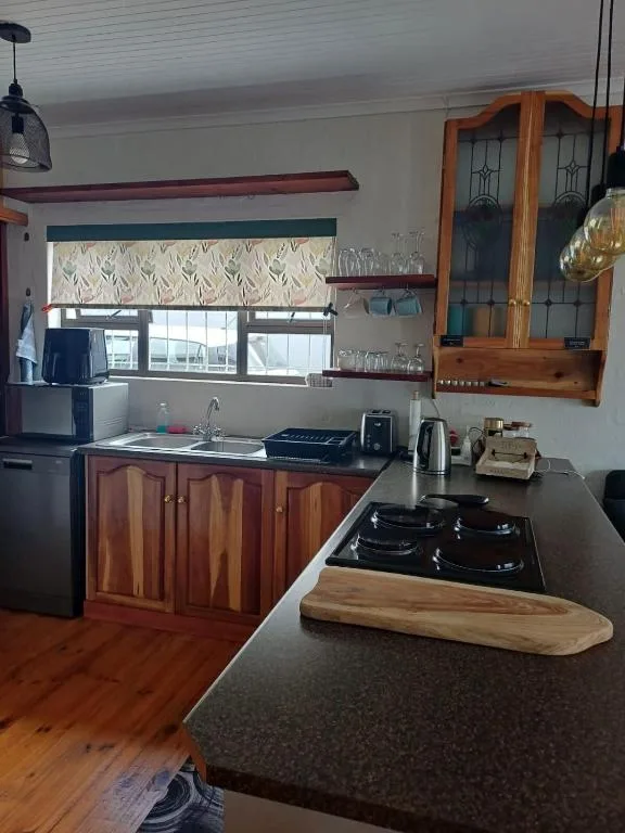 Modern kitchen with dark countertop, stove, wooden cabinetry, and window view